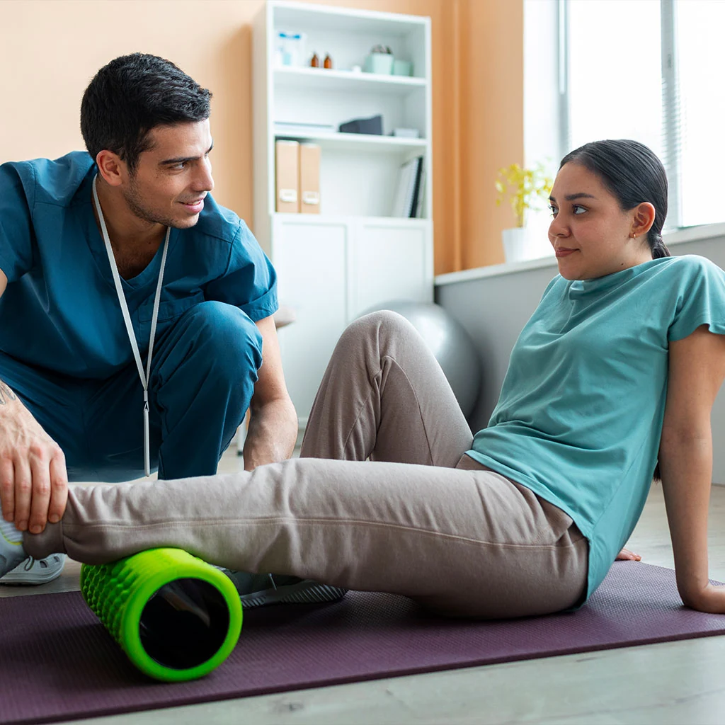 Physical therapist guiding a young athlete through a foam-roller leg rehabilitation exercise during a sports injury recovery session at Dynamic Physical Therapy