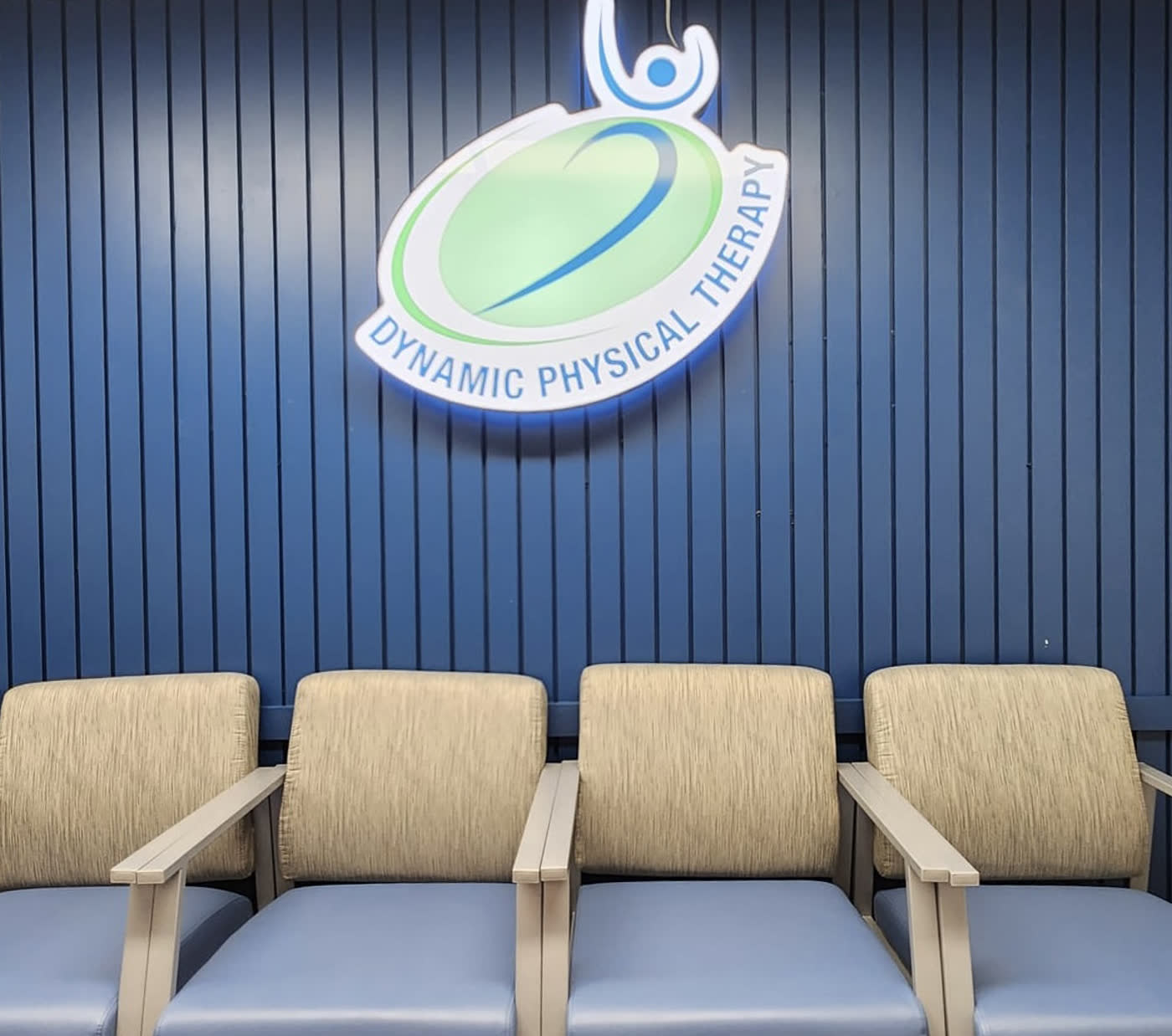 Patient seating beneath the backlit Dynamic Physical Therapy sign in the Flushing waiting area
